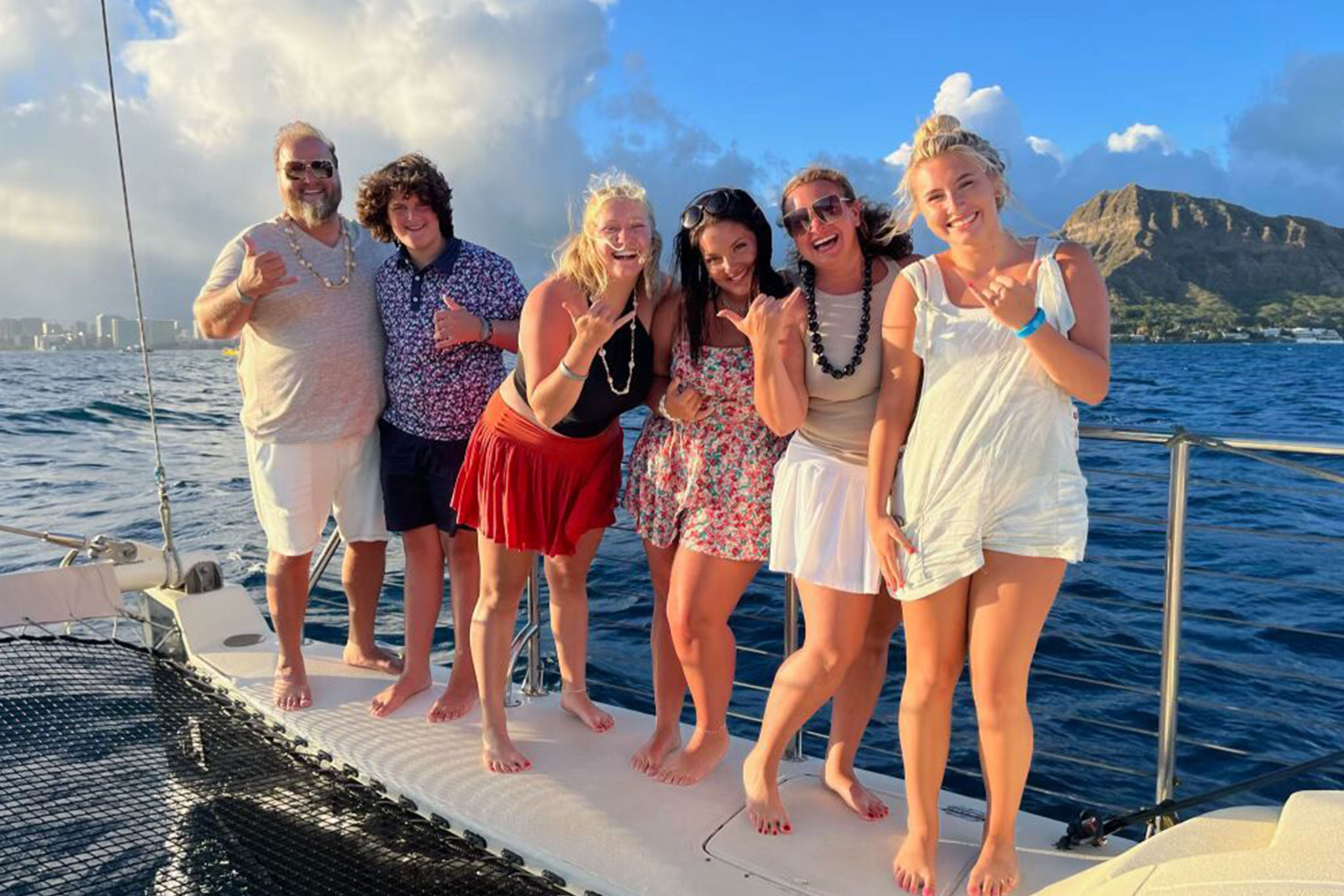 TaRanda’s family is on a boat deck in front of a beautiful coastal landscape, posing with shaka hand gestures.