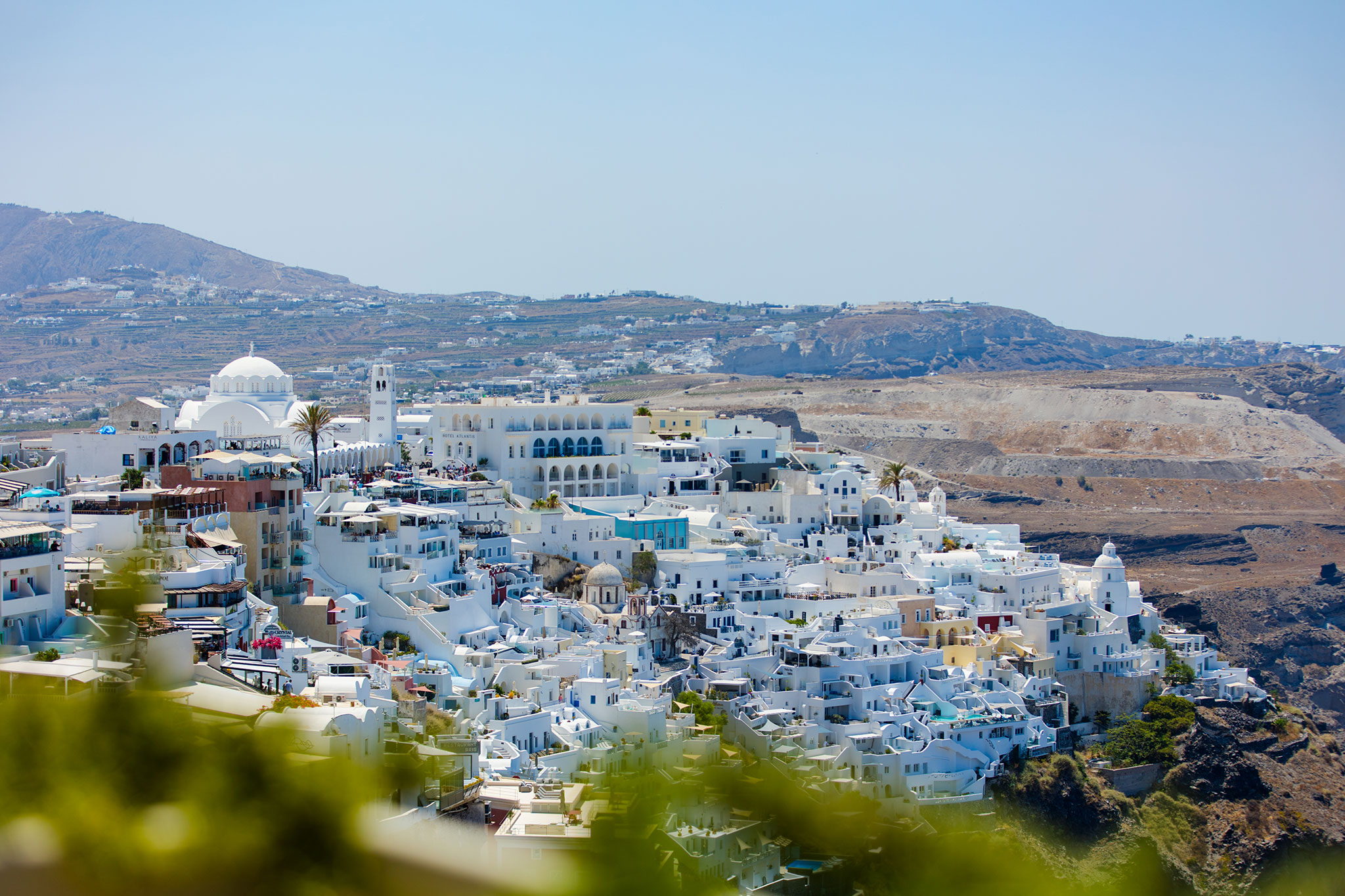 Scenic landscape of Fira town on Santorini Island, Greece, characterized by its traditional Cycladic architecture with white houses and blue domes amidst a rugged volcanic backdrop.