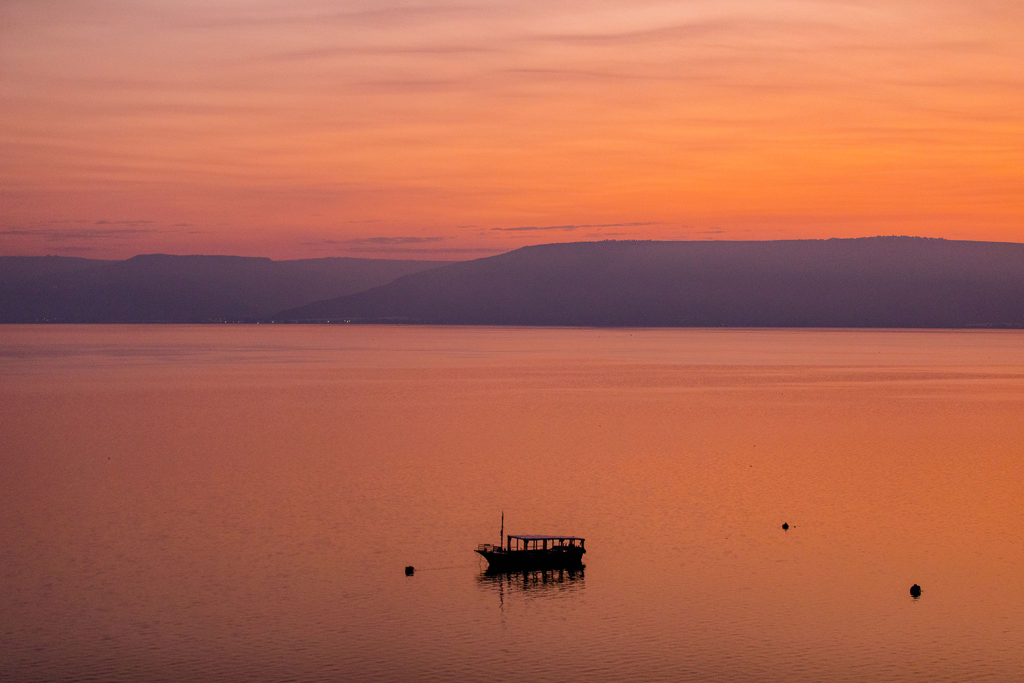 Silhouetted boat on a calm sea at sunrise with orange skies.