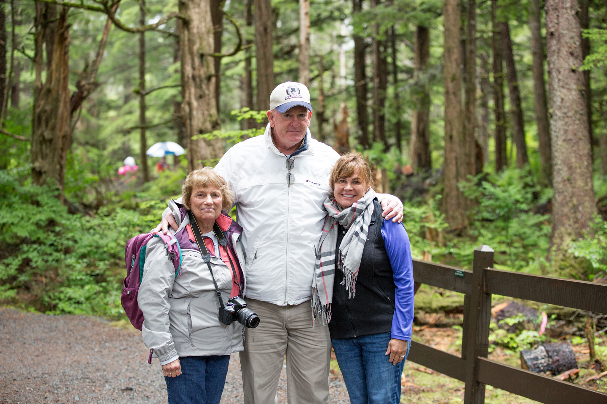 Outdoor portrait of two women and one man in casual outdoor gear, standing together on a wooded trail.