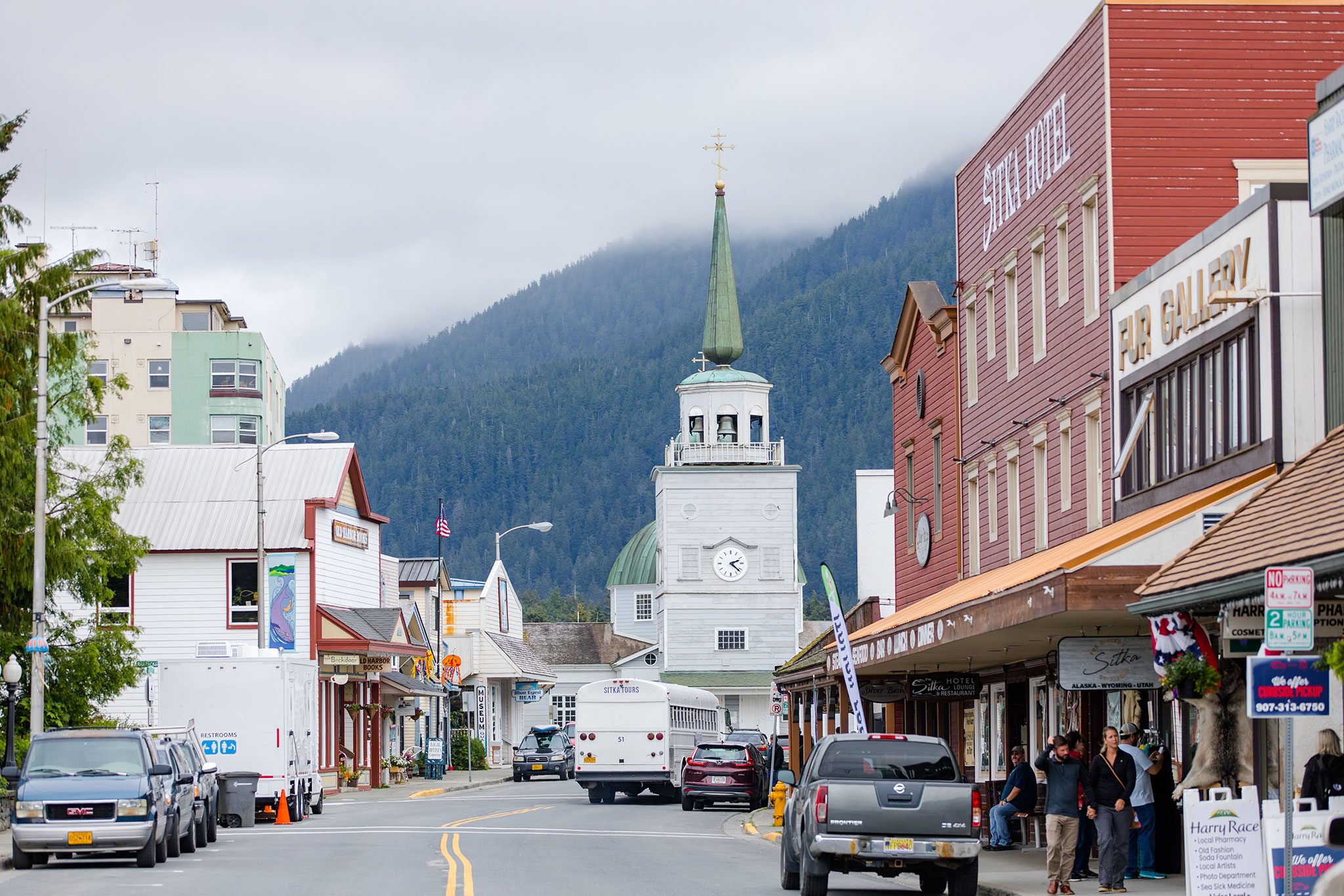 Small-town street scene with historic buildings and a church spire, set against a mountain backdrop.