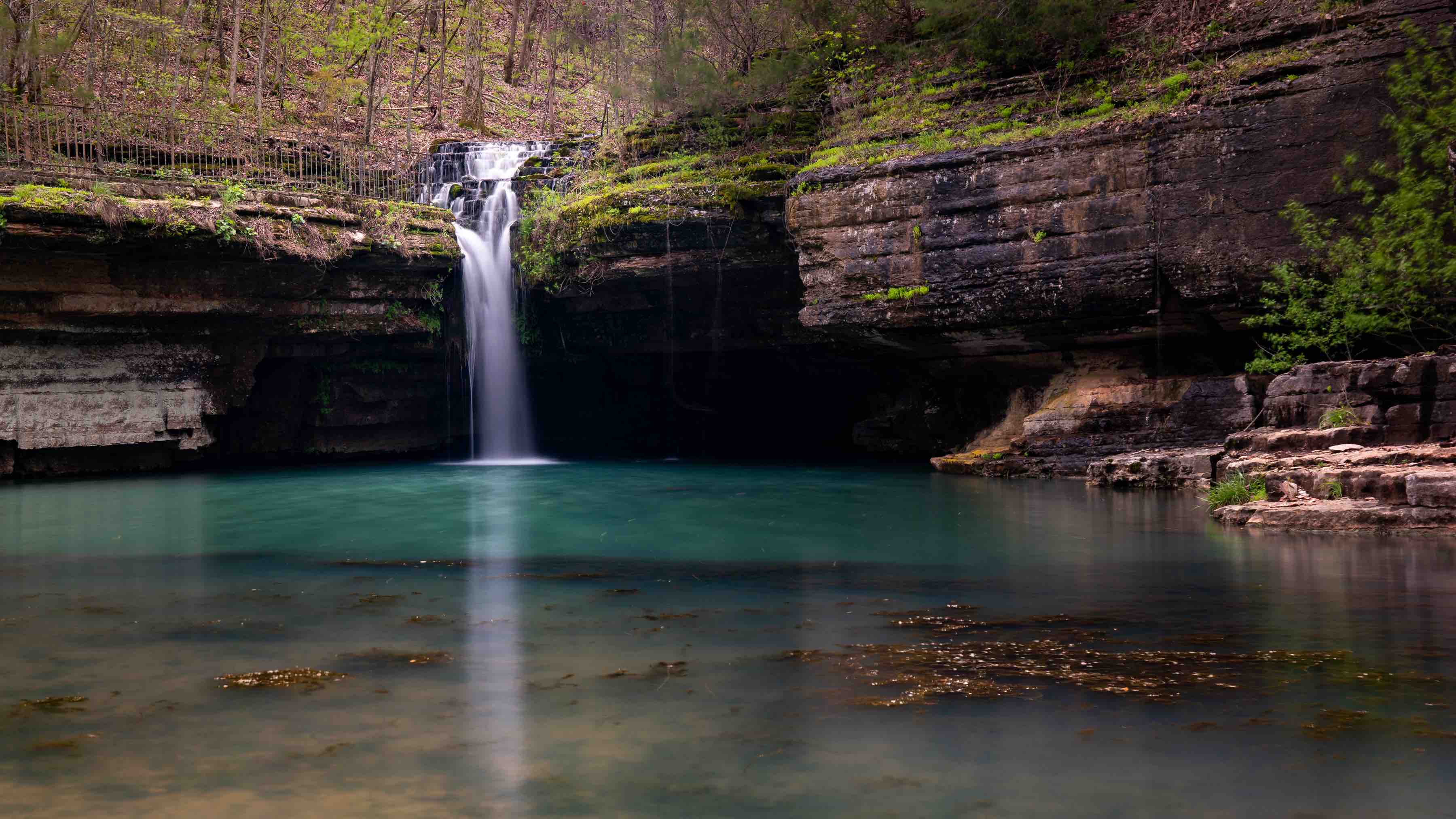 A waterfall falls into a blue-green lake surrounded by the mossy mountainside