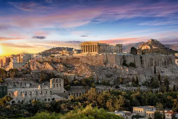 Sunset view of the Acropolis in Athens, Greece, highlighting the illuminated Parthenon and ancient ruins, surrounded by the city and mountains.